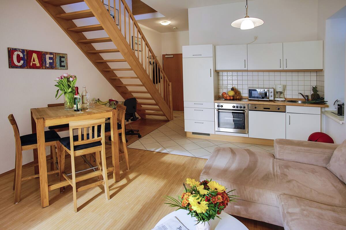 Una cocina moderna con armarios blancos, una mesa de comedor de madera y una escalera que sube a otro nivel.