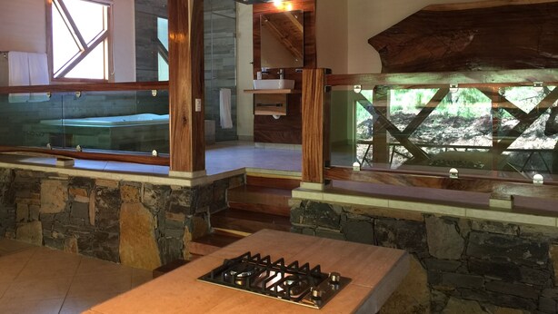 Una cucina rustica con un piano cottura a gas, travi in legno, pareti in pietra e un'ampia finestra vista su una zona boschiva.