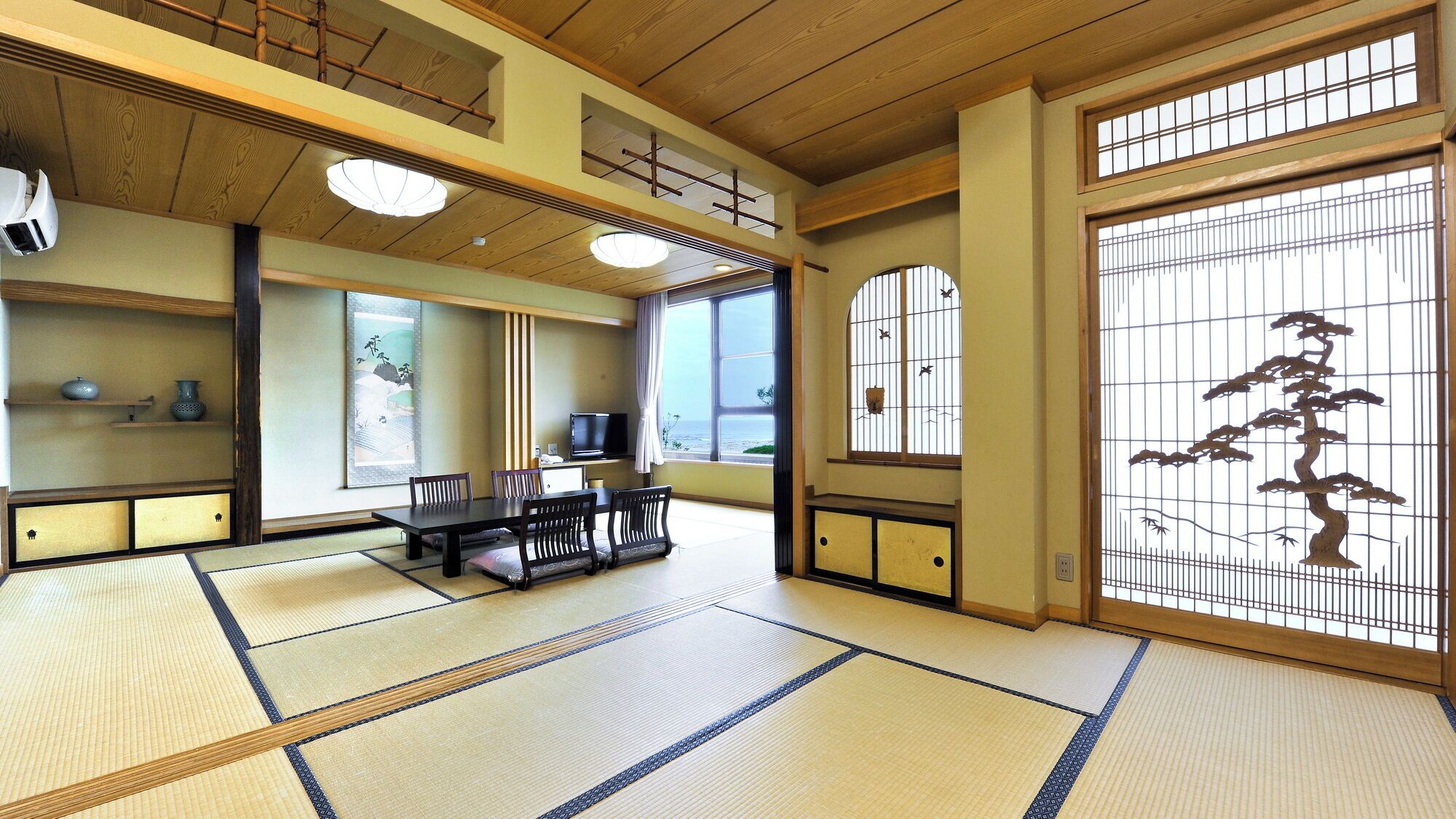 A tatami mat room with a low table, chairs, a TV, and a view through a shoji screen.
