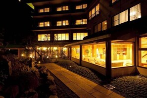 Ein mehrgeschossiges Gebäude mit beleuchteten Fenstern und einem gut einsehbaren Innenraum, das an ein Hotel oder eine Wohnanlage erinnert.