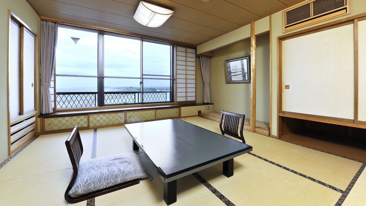 A tatami mat room with a low table, a chair, and a view through large windows.