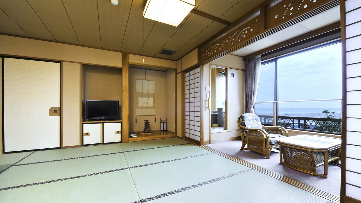 A traditional Japanese room with tatami flooring, a television, a sliding door, and a balcony with a view.