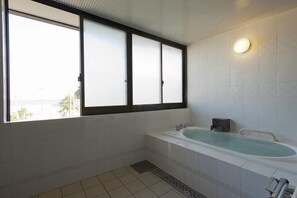 Ein modernes Badezimmer mit einer großen Badewanne, einem Fenster mit Milchglas und einer Wandleuchte.