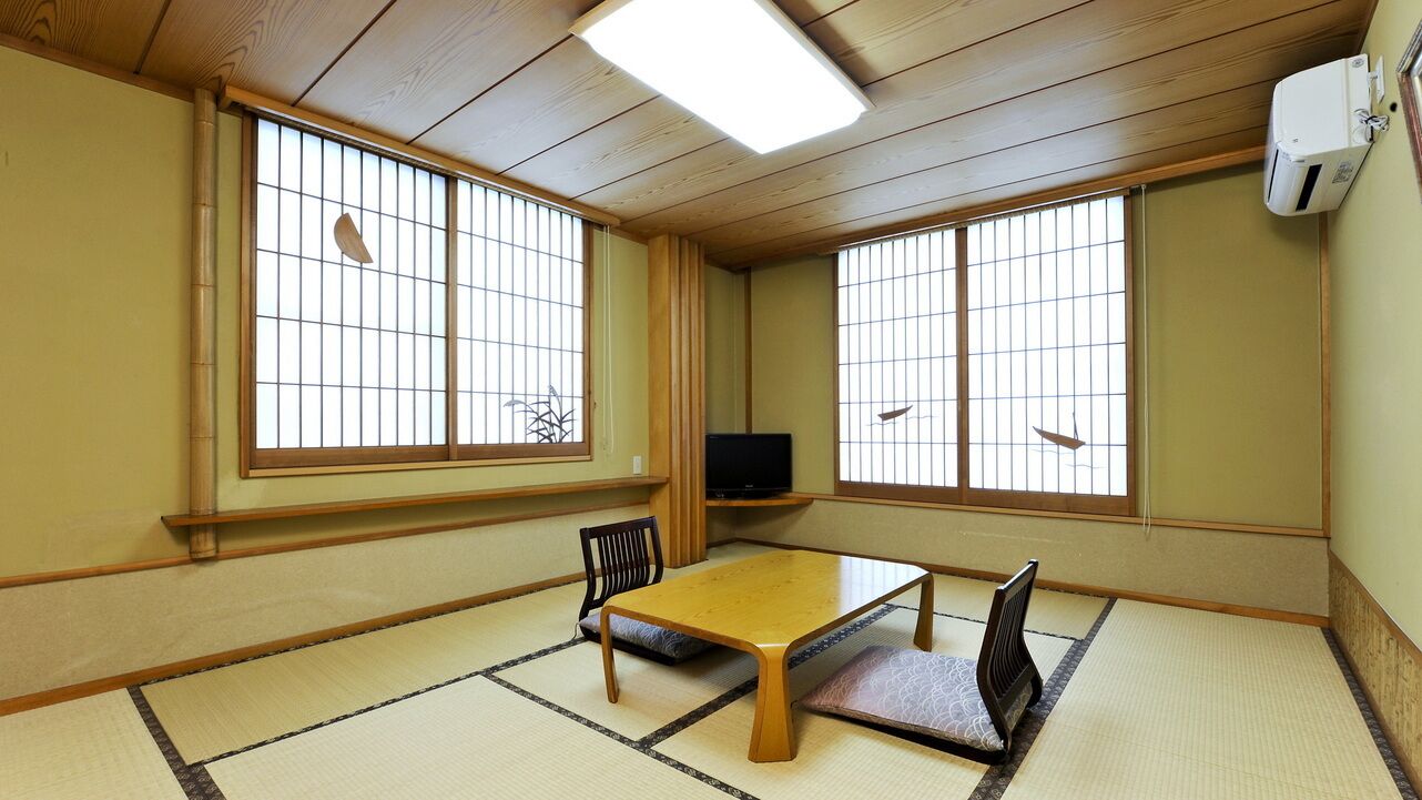 A traditional Japanese room with tatami flooring, a low table, chairs, and sliding doors with windows.