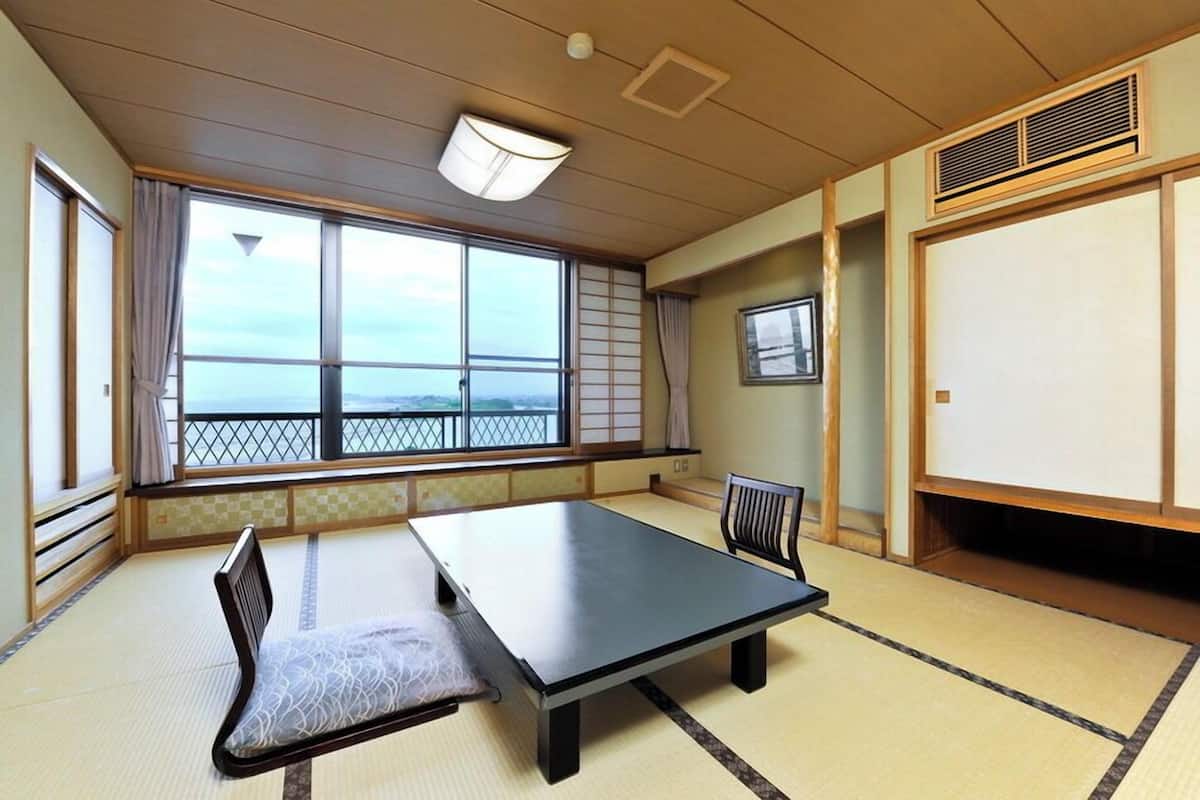 Un espacio con esteras de tatami, una mesita baja y asientos, ventanas amplias con vistas, y puertas correderas tradicionales japonesas.