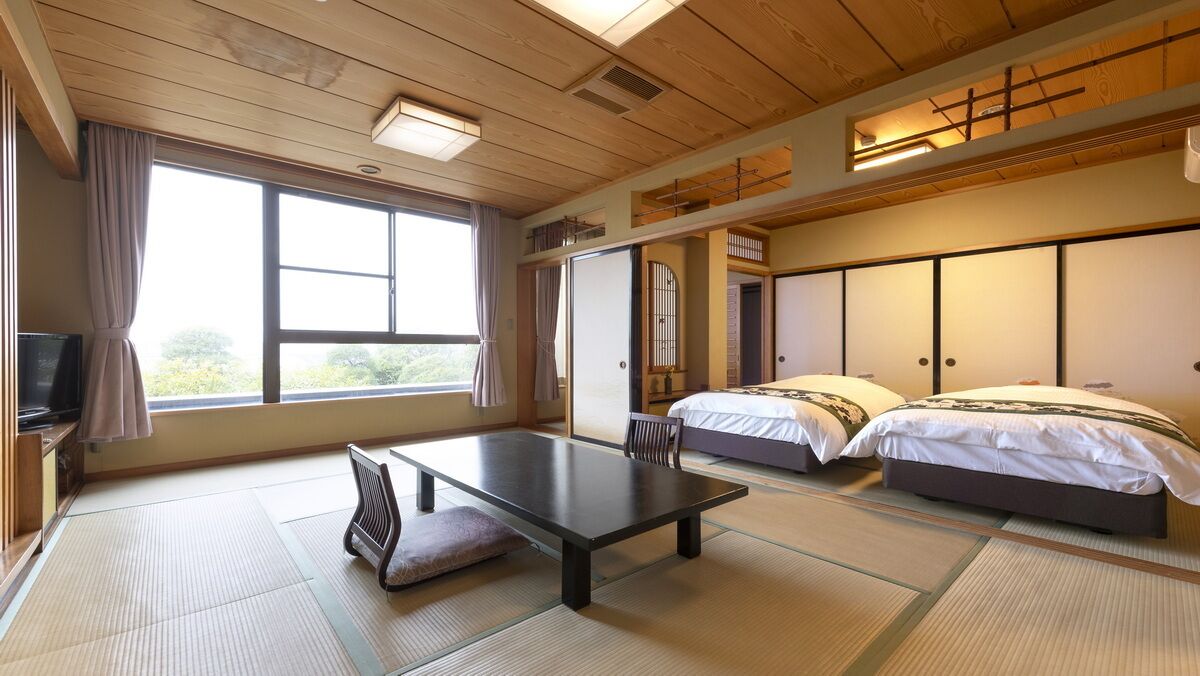 Una habitación japonesa tradicional con suelo de tatami, una mesa baja, dos camas y una puerta corredera.