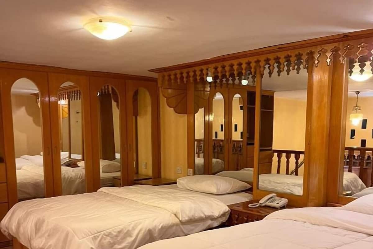 Une chambre d’hôtel avec trois lits simples, des têtes de lit en bois et un grand miroir.