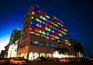 Un hôtel à plusieurs étages, doté d’une rangée de balcons, chacun éclairé par une lumière d’une couleur différente.