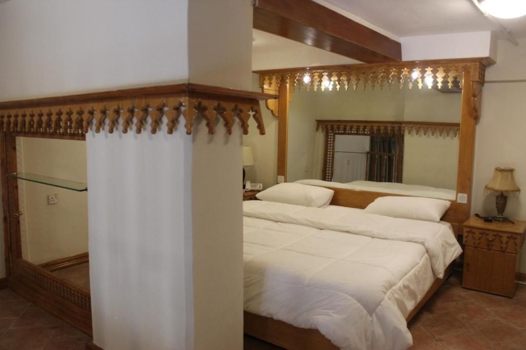 A bedroom with a large bed, a wooden headboard, a nightstand, and a mirror.