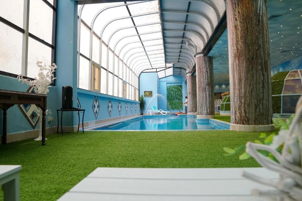 Piscina interna com teto curvo, grama sintética e pilares de madeira.