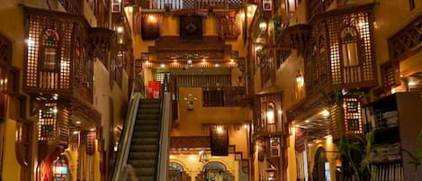 Un interior de varios niveles con balcones de madera ornamentados, una escalera central y un candelabro.