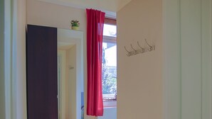 A hallway with a large mirror, a red curtain, and a window with a view of greenery. - Ferienwohnungen Eicher Wachtlerstraße (Rostock)