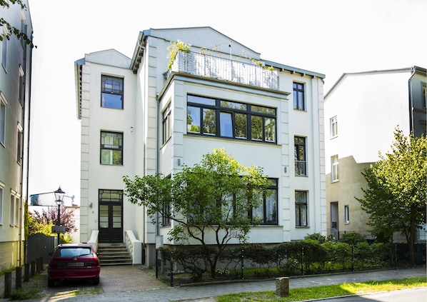 A modern two-story building with a white facade, large windows, and a visible balcony.