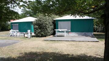 Two green tents with white roofs, a table, and chairs outside.