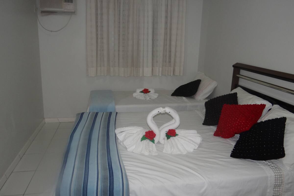 A hotel room with a bed, a bench, and a window with curtains.