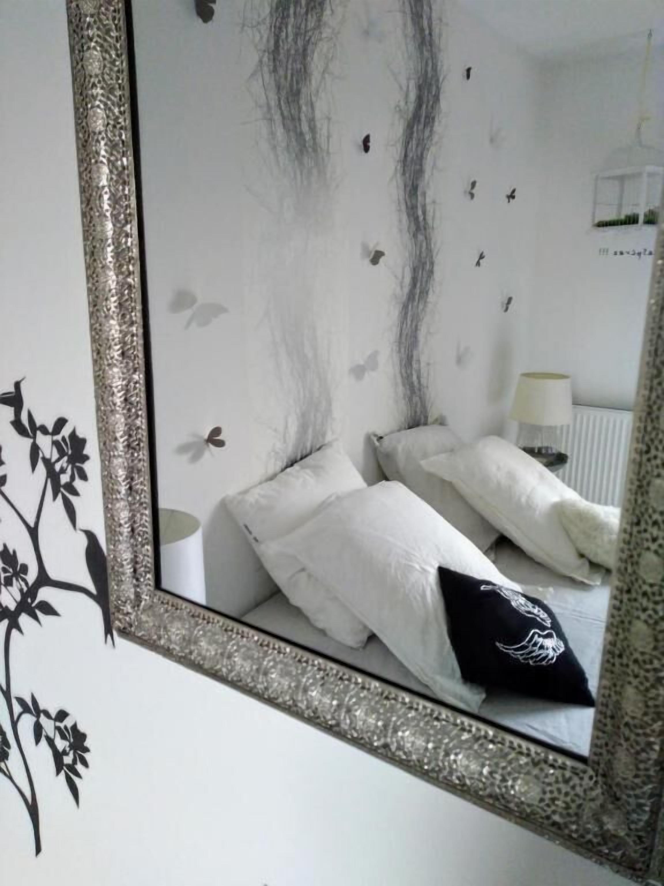 Een slaapkamer met een grote spiegel, wit beddengoed en een muursticker met vogels.