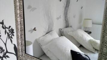 Een slaapkamer met een grote spiegel, wit beddengoed en een muursticker met vogels.