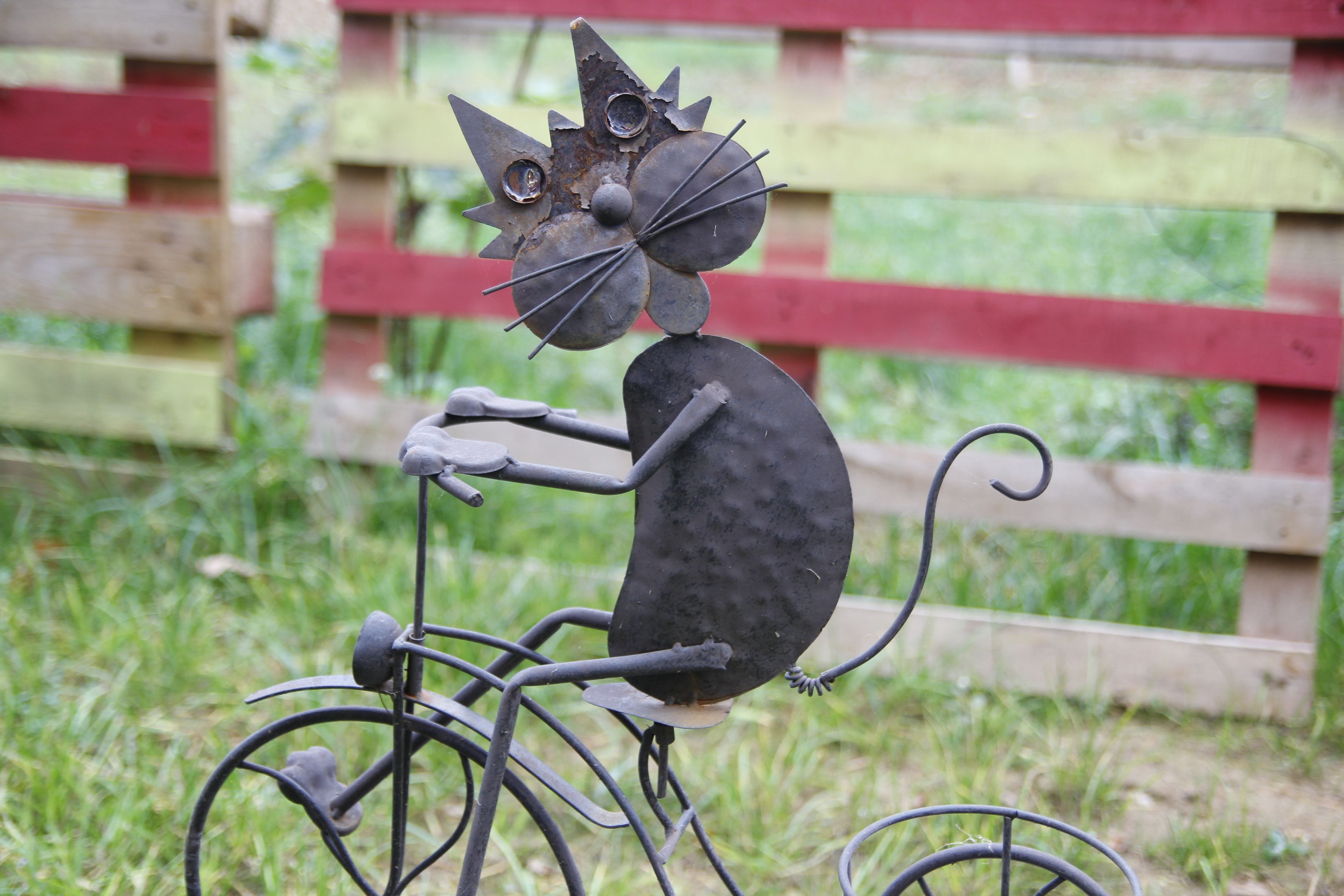 A metal sculpture of a cat riding a bicycle.