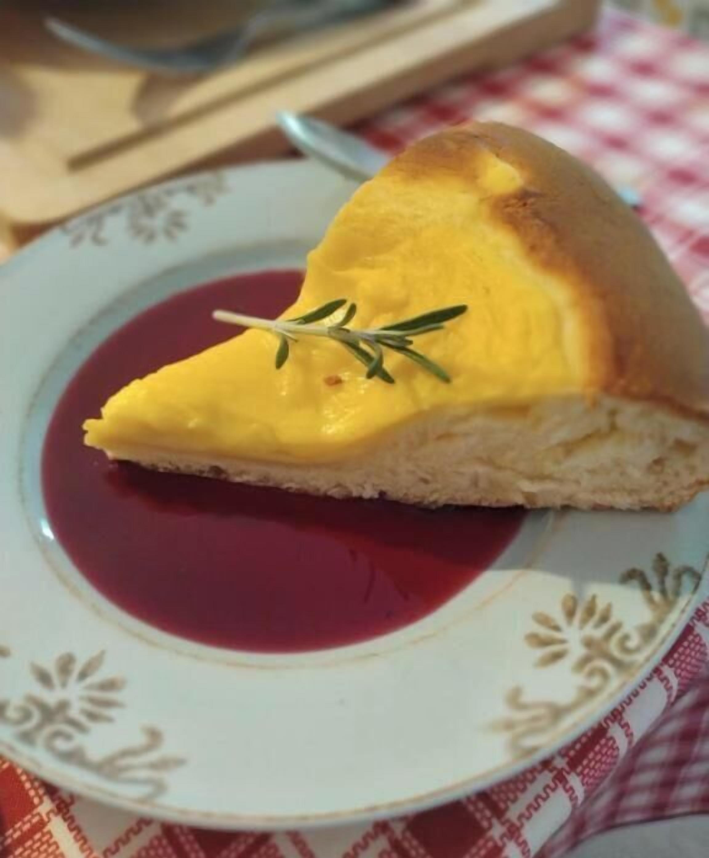 A slice of pie with a sprig of rosemary on a plate with a red sauce.