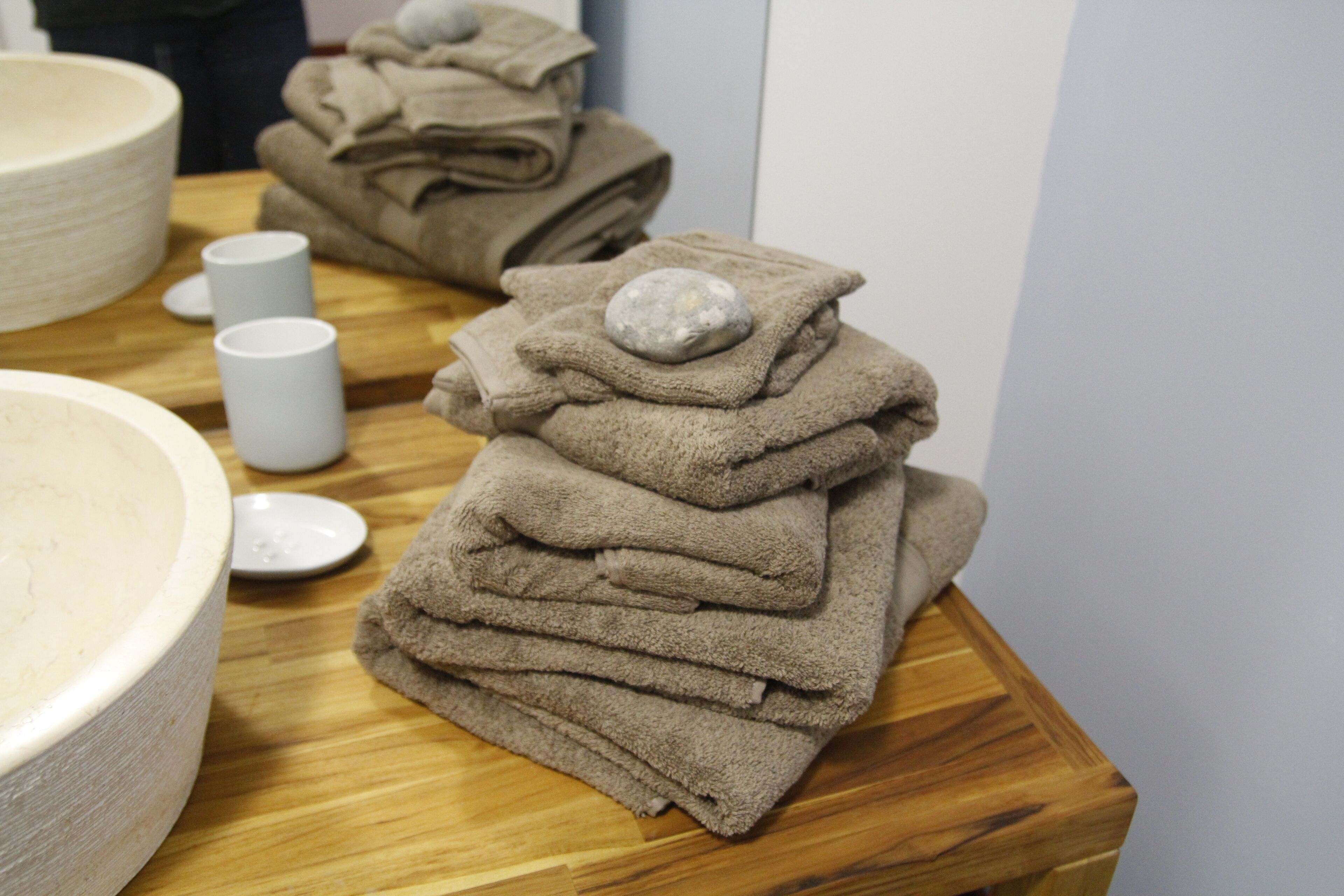 A stack of folded towels on a wooden table with a bowl and a cup in the background.