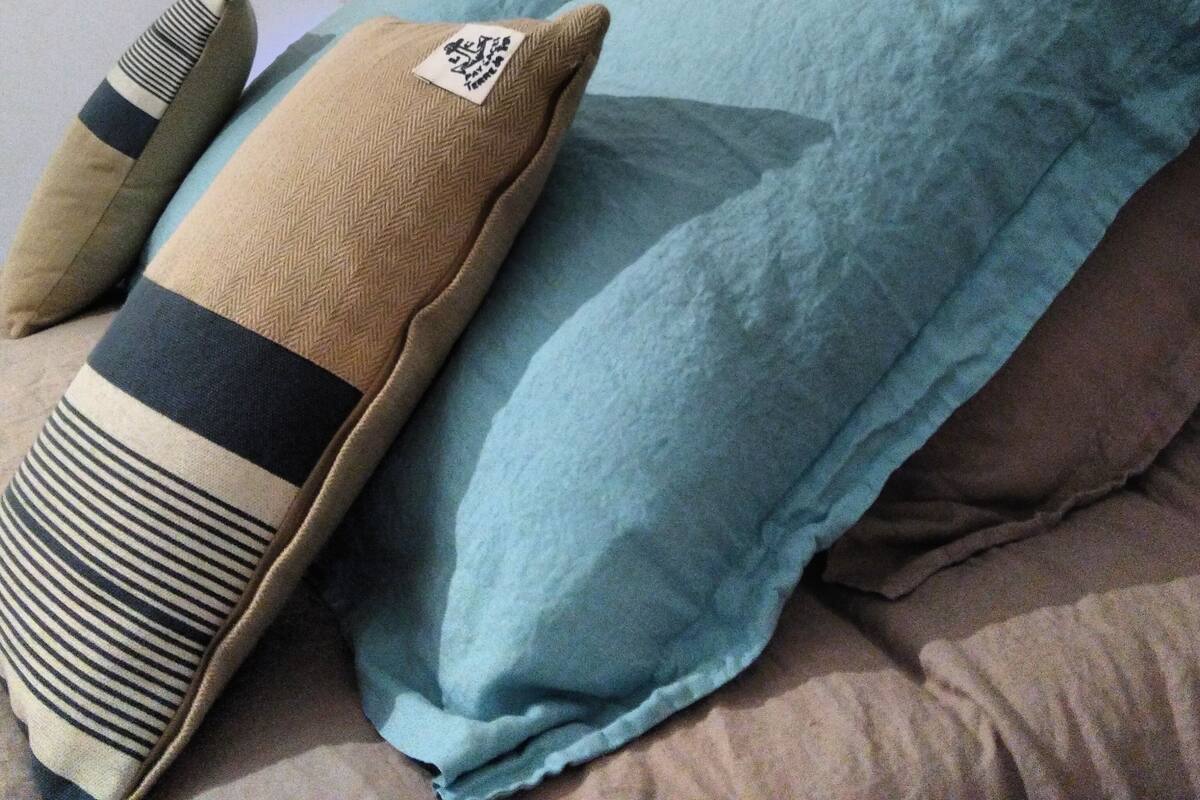 A bed with a blue blanket and two pillows, one striped and one with a herringbone pattern.