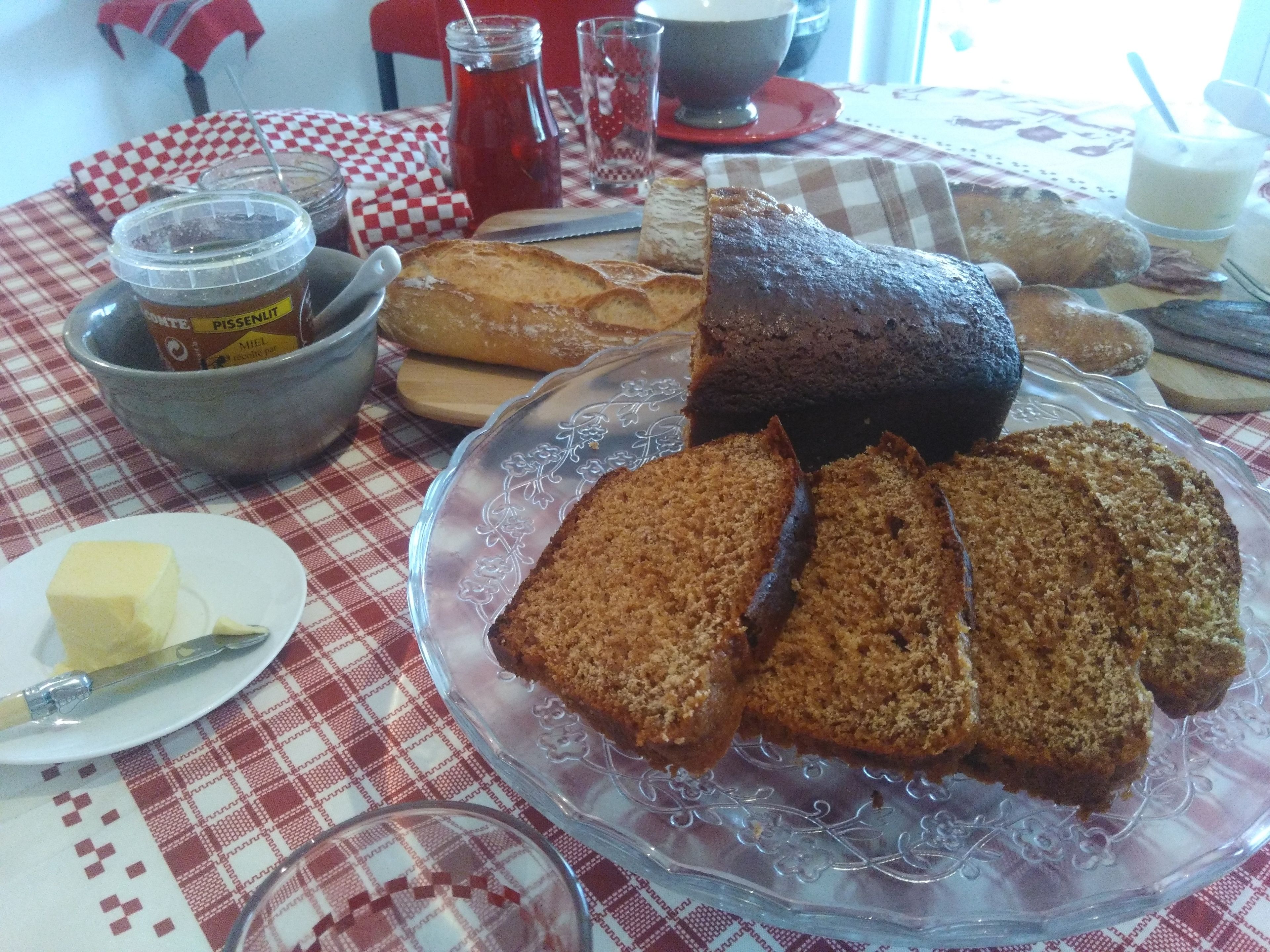A table with a variety of breads and pastries, a bowl of jam, and a glass of milk.