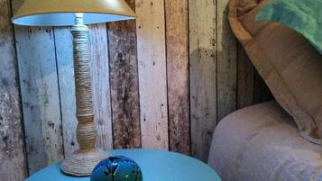 A room with a round table, a lamp, and a bed against a wooden wall.