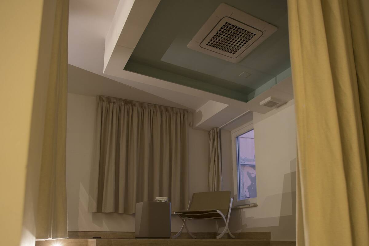 A modern bathroom with a glass-enclosed bathtub, beige walls, and a window with curtains.