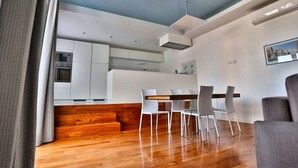 A modern kitchen with white cabinets, a built-in oven, and a dining area with a wooden table and white chairs. - B&B La Gaetana (Gaeta)