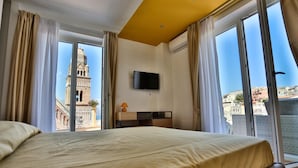 A hotel room with a bed, a TV mounted on the wall, and a view of a historic tower through large windows. - B&B La Gaetana (Gaeta)