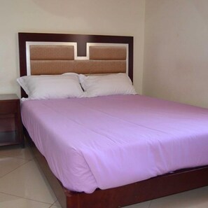 Una cama bien hecha, con cabecera de madera y colcha morada.