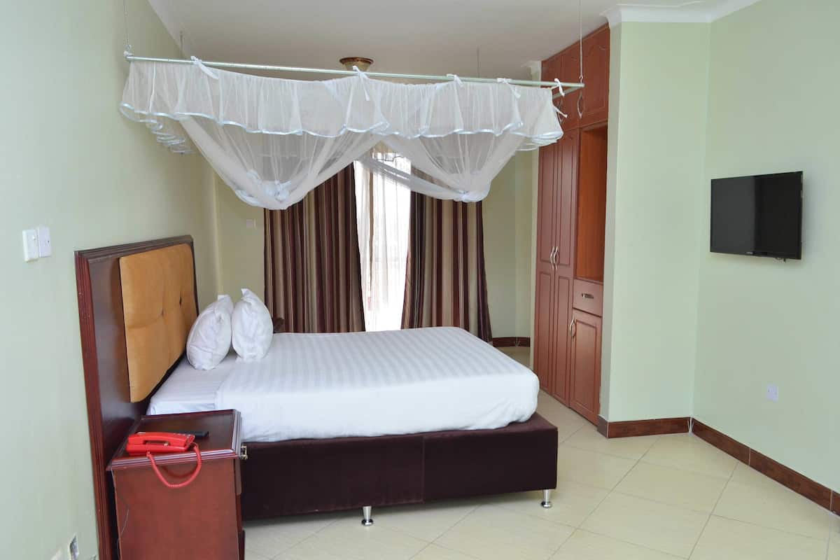 A bedroom with a bed, a bedside table with a red object, a wardrobe, and a TV on the wall.