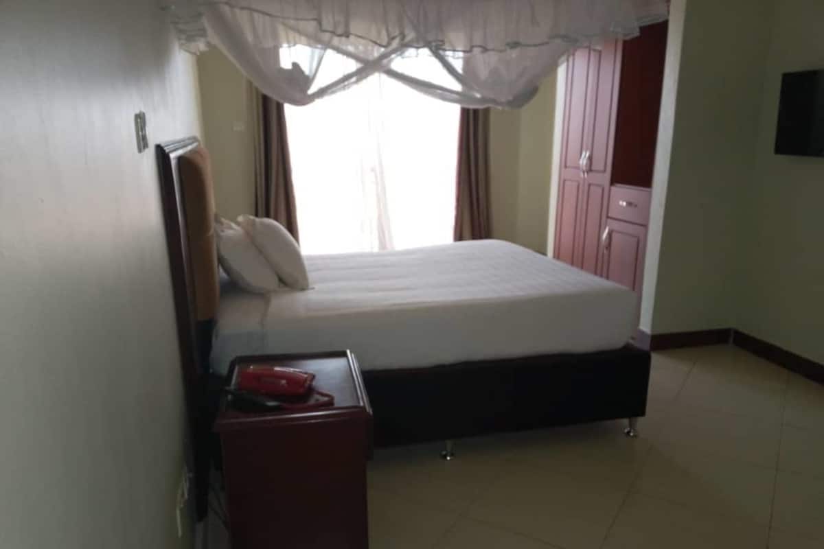 A bedroom with a bed, a nightstand, a wardrobe, and a television on the wall.