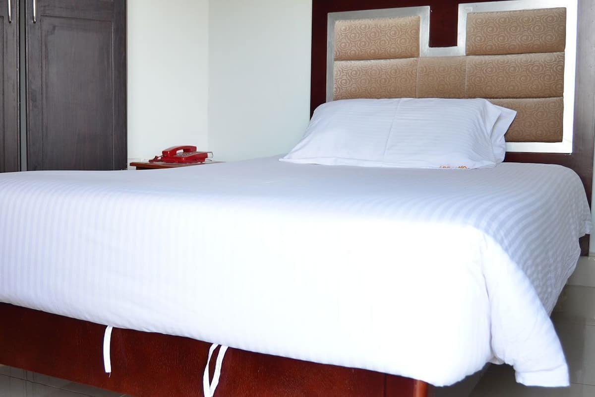A neatly made bed with a wooden headboard, a dark wooden wardrobe, and a red telephone on the nightstand.