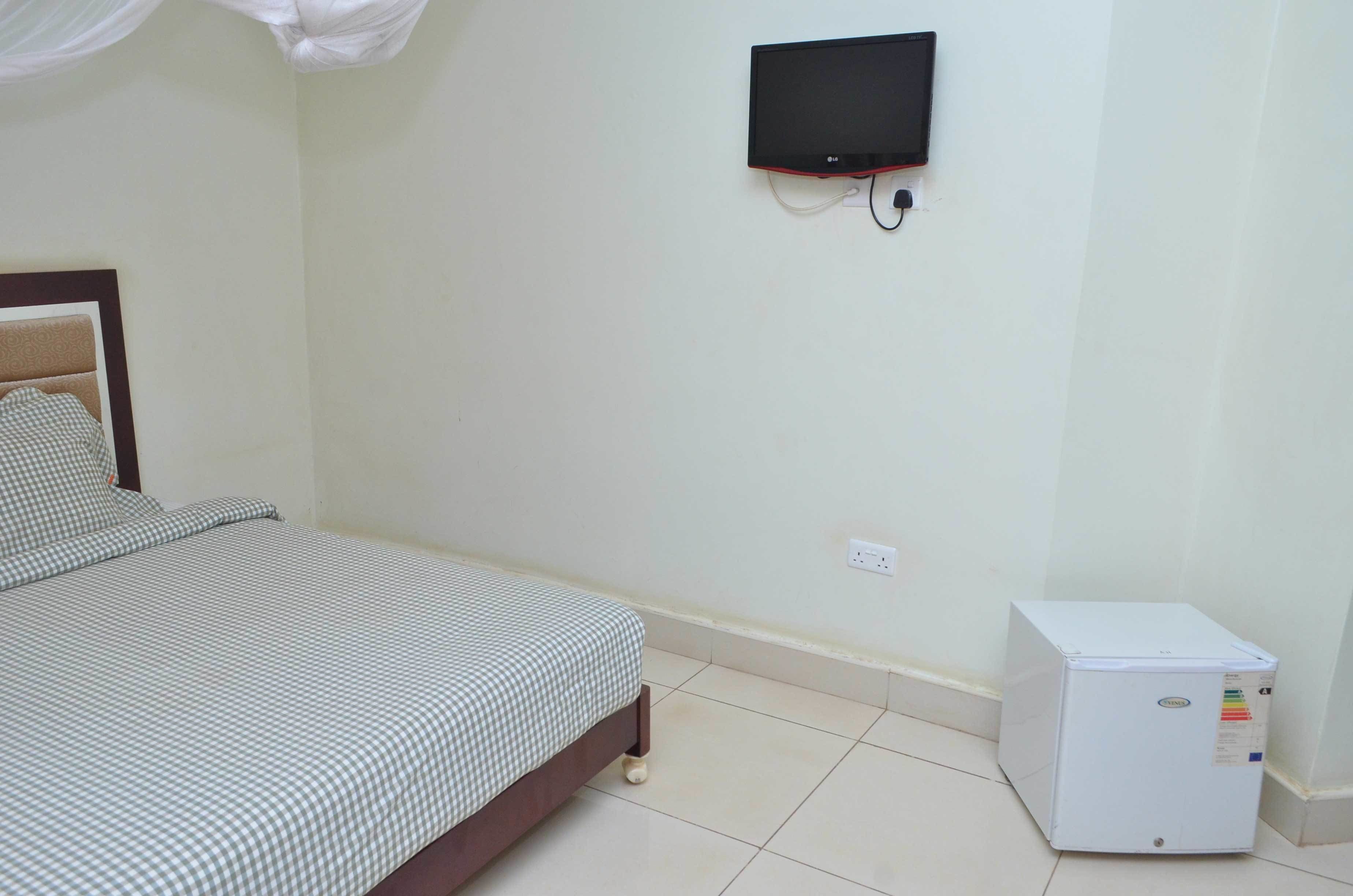 A bedroom with a bed, a television mounted on the wall, and a small white appliance on the floor.