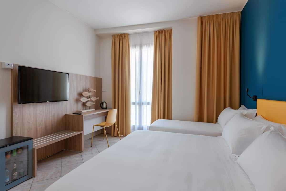 Una habitación de hotel con cama, escritorio, silla, televisor y minibar.