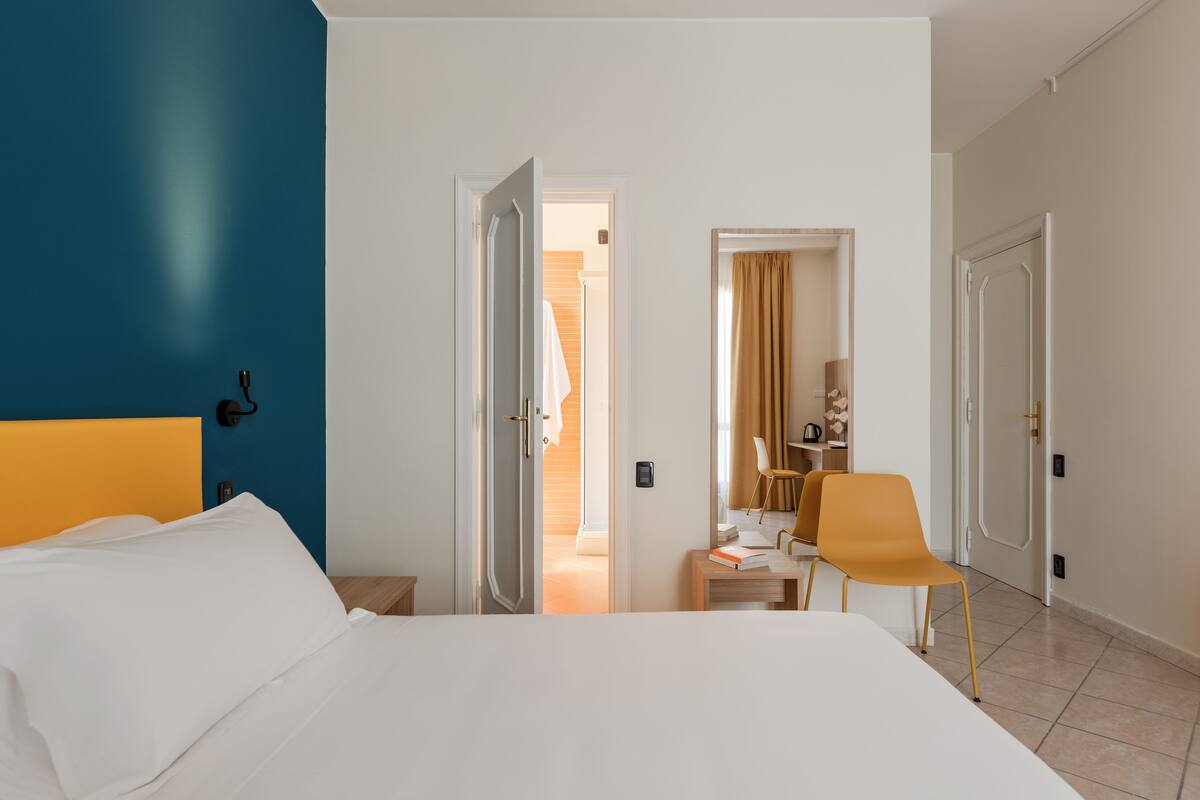 Habitación de hotel con cama, escritorio y silla. Se ven puertas que dan a otras habitaciones y al baño.