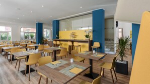 Um restaurante moderno com cadeiras amarelas e mesas de madeira, uma área de bar e janelas amplas.