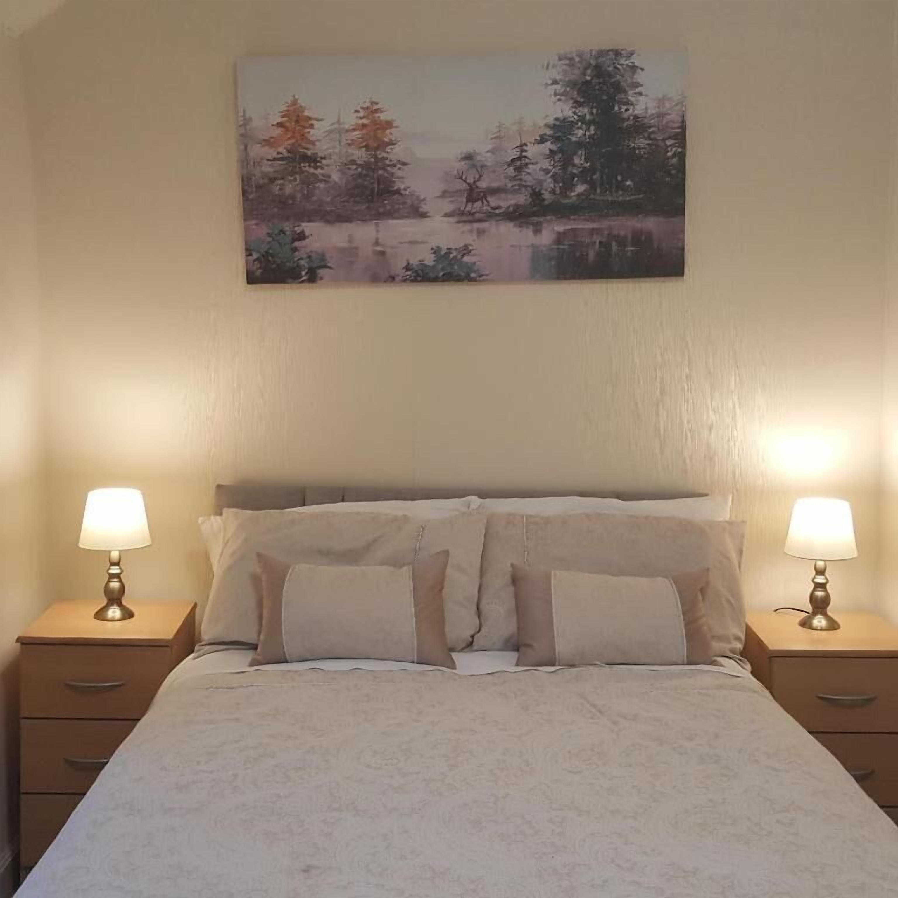 A bedroom with a bed, two bedside tables, and a painting on the wall.
