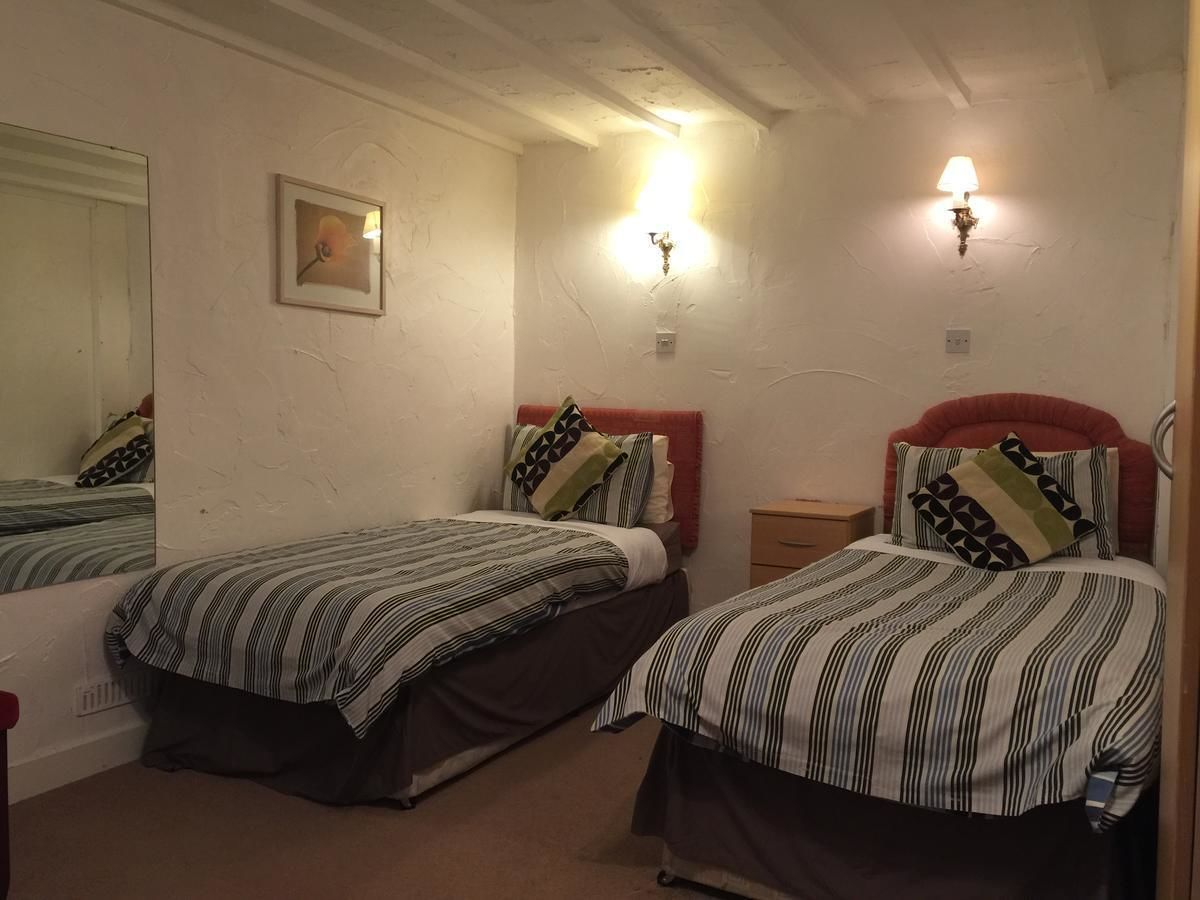 A room with two single beds, each with striped bedding and patterned pillows. There are wall-mounted light fixtures and a framed picture on the wall.