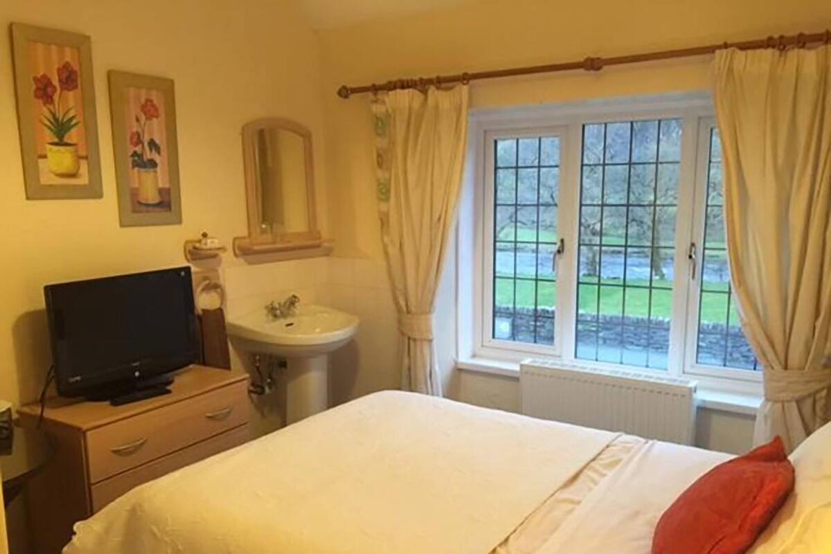 A bedroom with a bed, a television on a dresser, a sink, and a window with curtains.