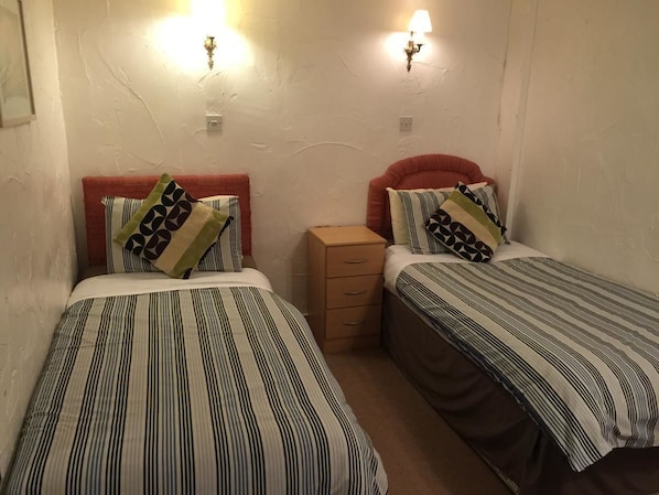 A room with two single beds, each with striped bedding and patterned pillows. There is a small wooden nightstand between the beds. - The Dragon Hotel and Restaurant (Betws-Y-Coed)