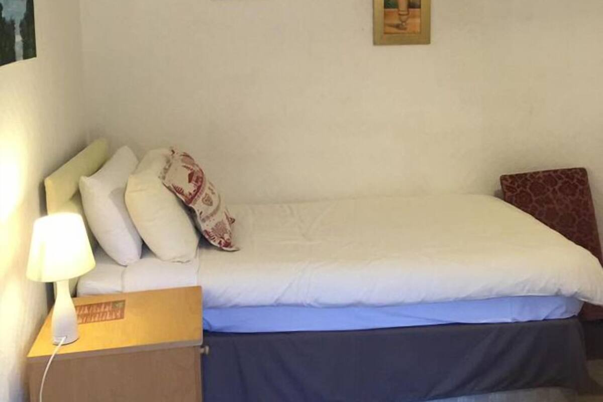 A bedroom with a bed, pillows, a bedside table with a lamp, and two framed pictures on the wall.