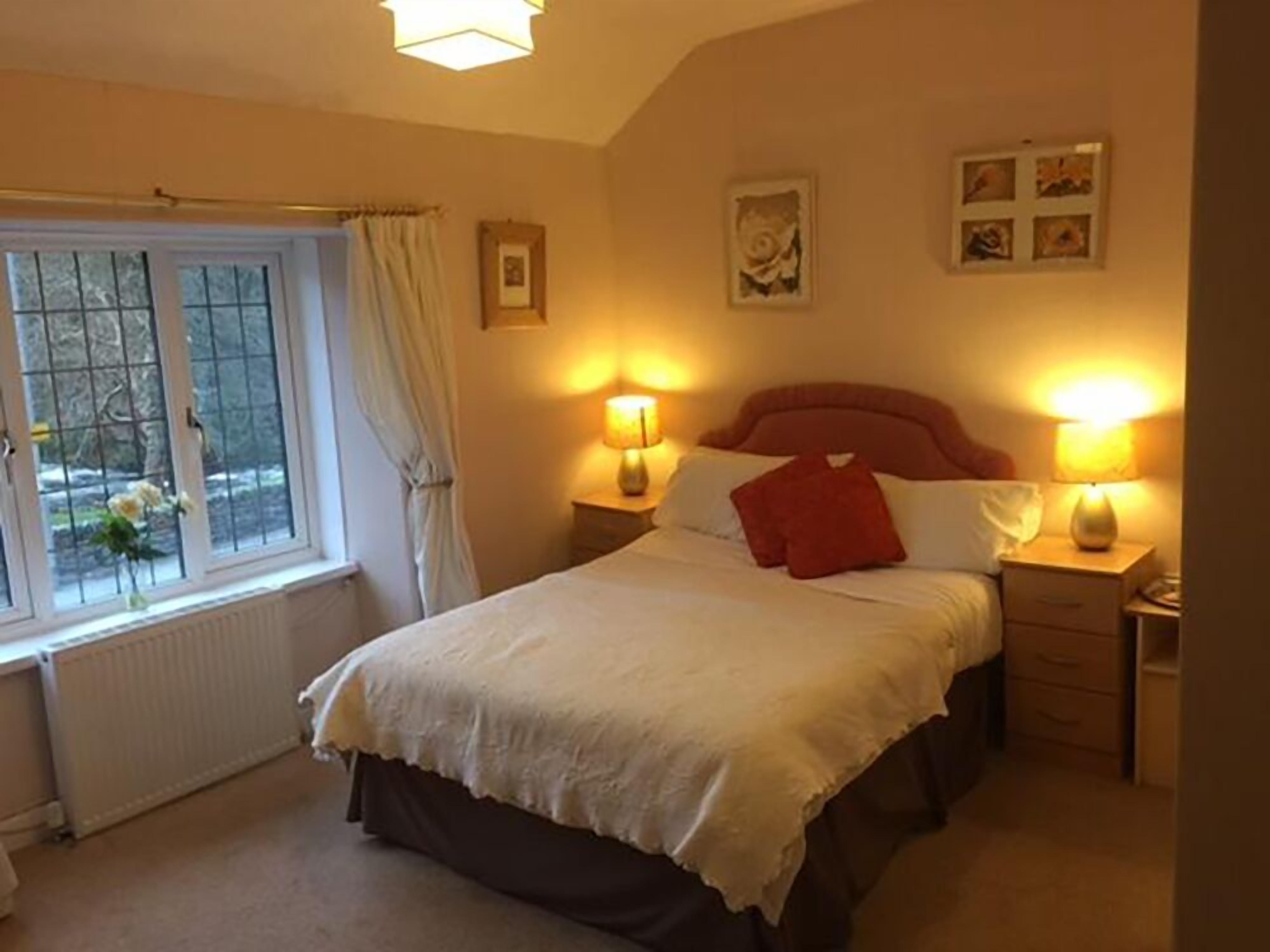 A bedroom with a bed, two bedside tables, a window with curtains, and wall-mounted artwork.