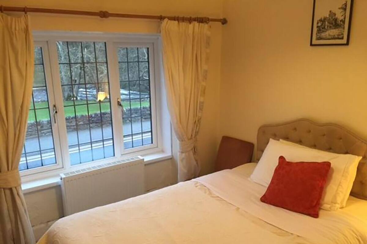 A bedroom with a bed, a window with curtains, a radiator, and a picture on the wall.