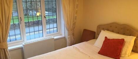 Un dormitorio con cama, ventana con cortinas, radiador y un cuadro en la pared.