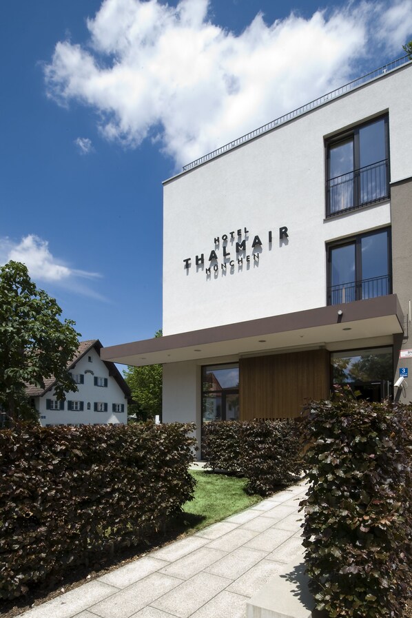 A modern hotel building with a clear sky and well-maintained hedges. - Hotel Thalmair (Munich)