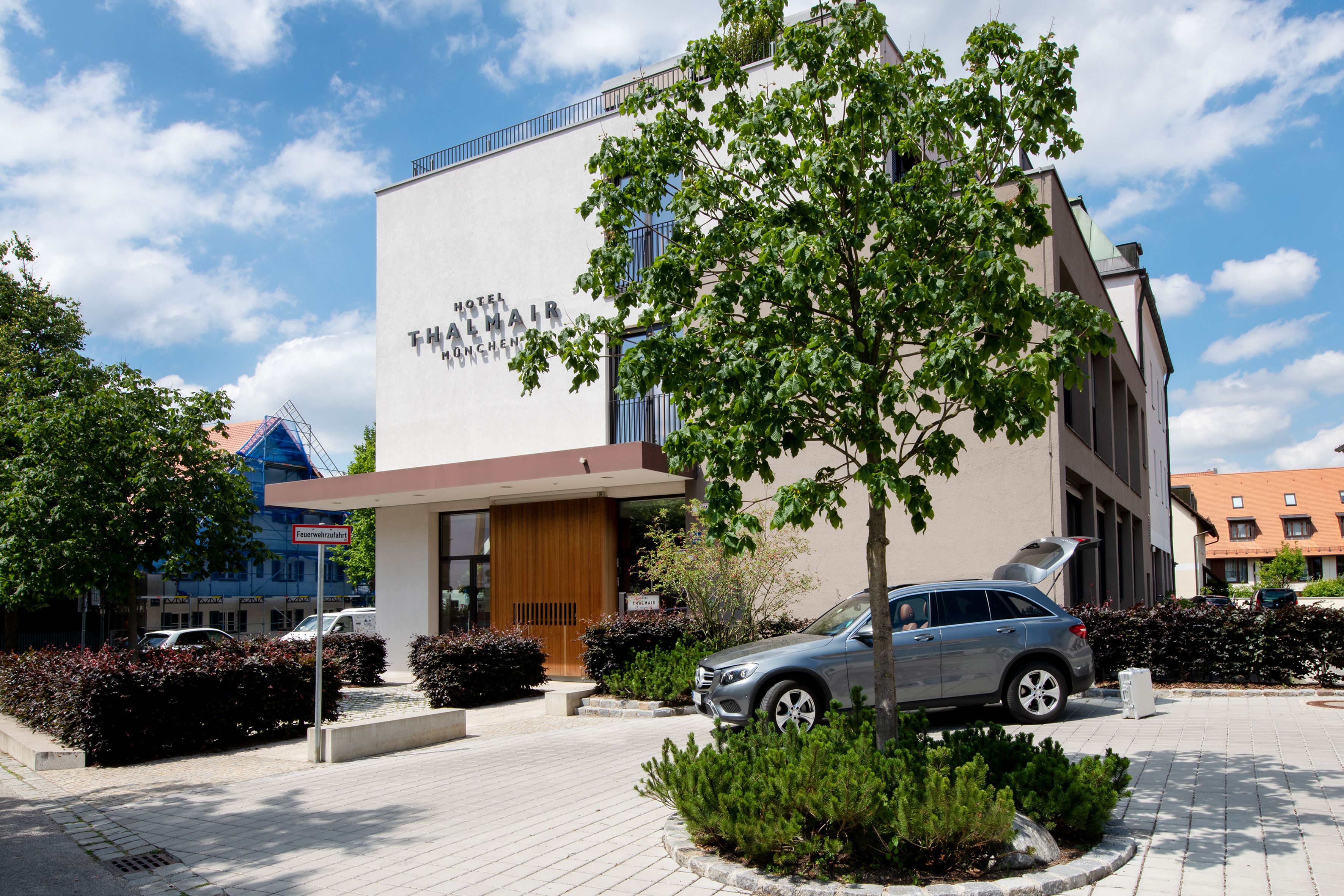 A hotel with a modern facade, a car parked in front, and a tree in the center.