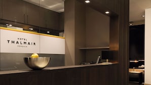 Uma área de recepção com design moderno, incluindo um balcão de atendimento, uma tigela com um limão e uma placa indicando Hotel Thalmair em Munique.