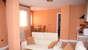 A living room with a white sofa, a wooden coffee table, and a dining area with a table and chairs. - Aparthotel Capitolina (Merida)